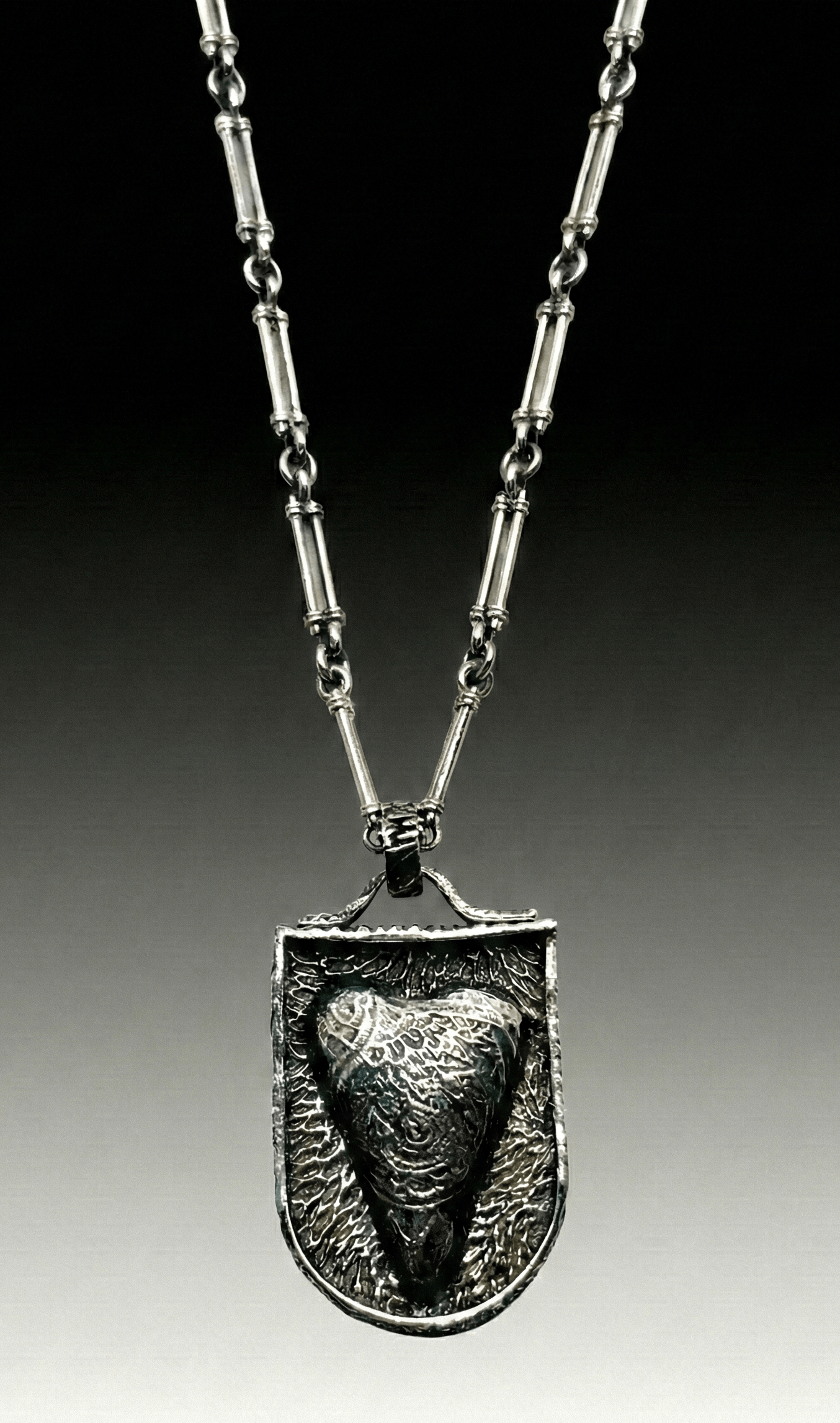 Silver pendant necklace featuring a textured heart-shaped charm, showcasing intricate designs. Ideal for discussions on jewelry design or fashion accessories.