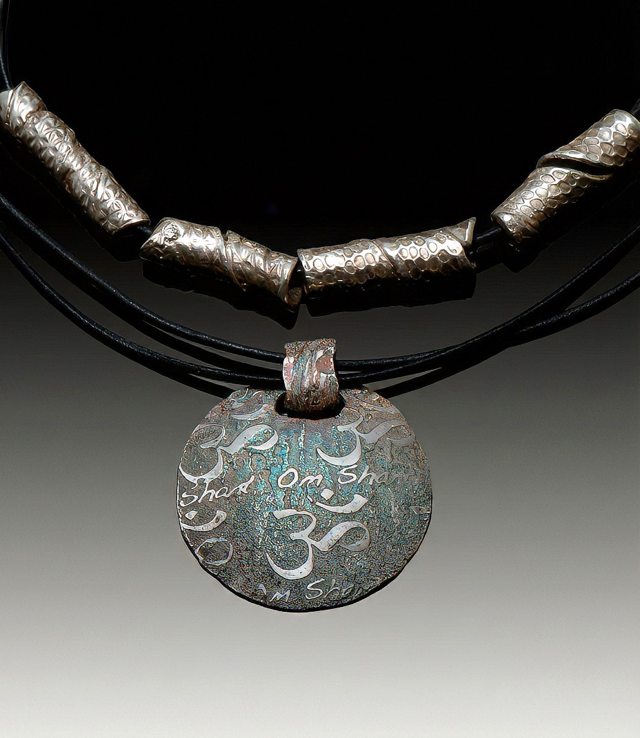 Silver pendant necklace featuring intricate designs and symbols, including "Om" and "Shanti," on a dark leather cord.