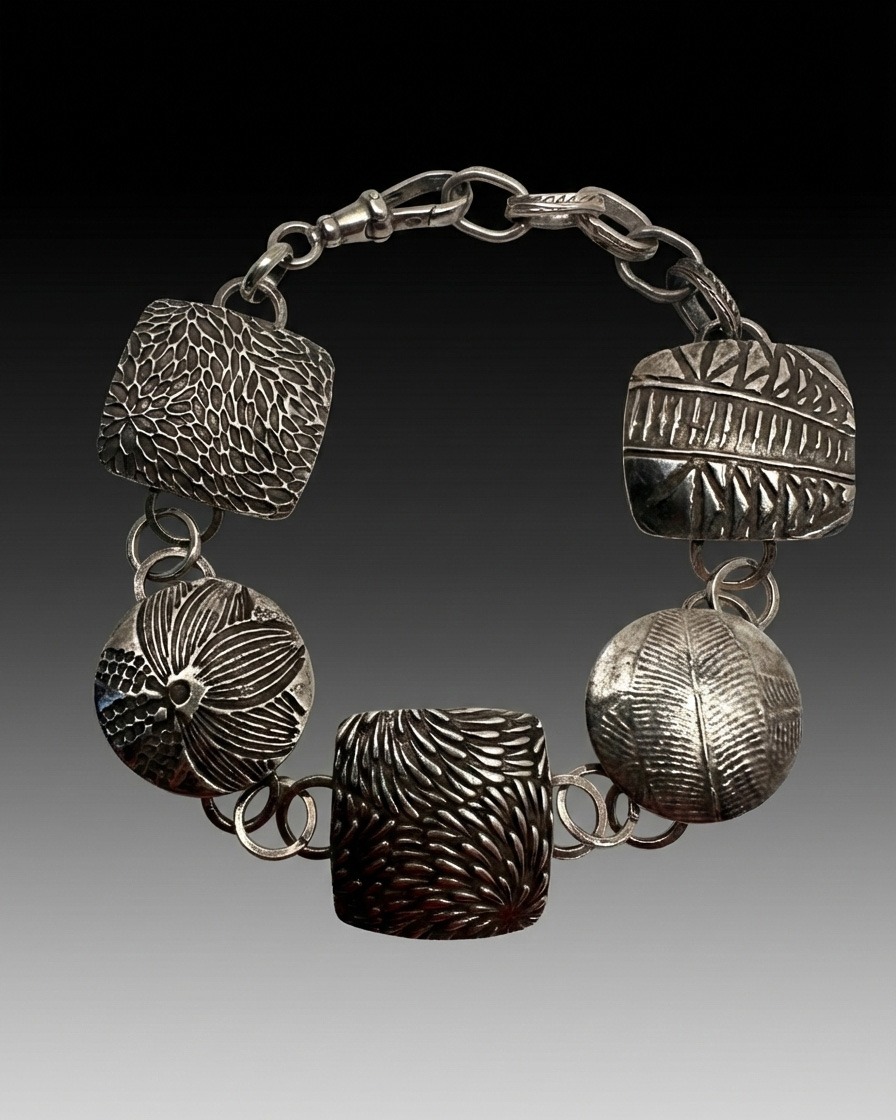 Silver bracelet with textured, geometric charms linked in a circle. Designs include leaf patterns and abstract motifs, set against a dark gradient background.